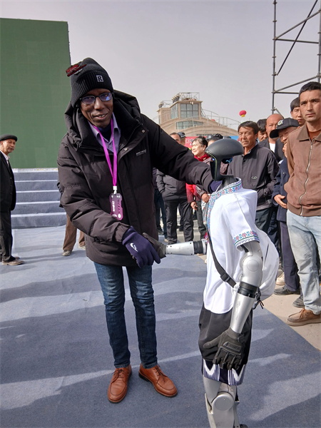 Aliu Baldé interagit avec un robot humanoïde lors de la cérémonie d'ouverture de la 11e Foire des fruits spécialisés du Xinjiang (Aksu), dans la région autonome ouïgoure du Xinjiang (nord-ouest de la Chine). (Photo fournie par la personne interviewée)